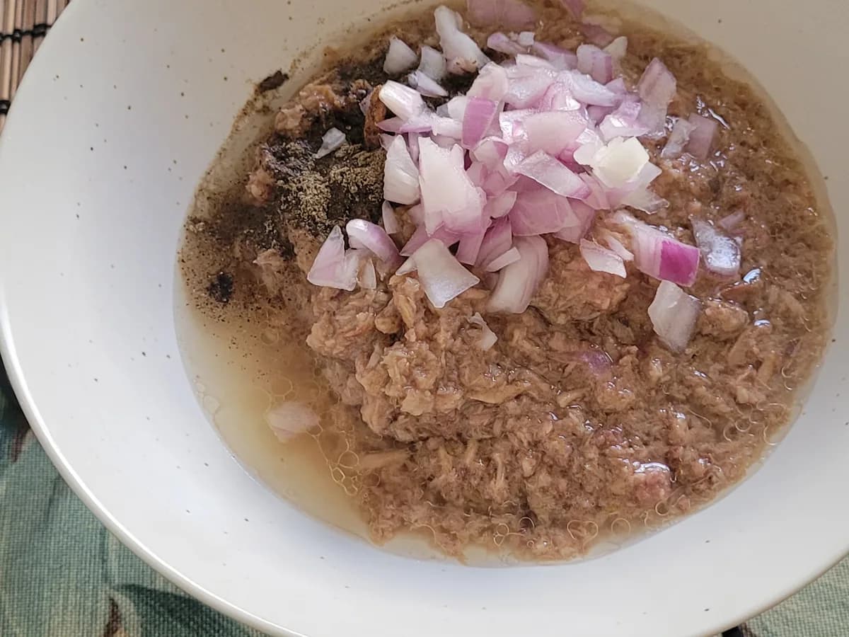 Drained tuna with chopped onion, black pepper, and salt in a bowl
