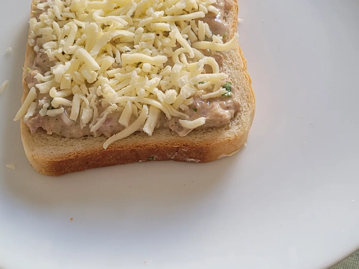 Shredded cheese added over tuna filling on sandwich bread